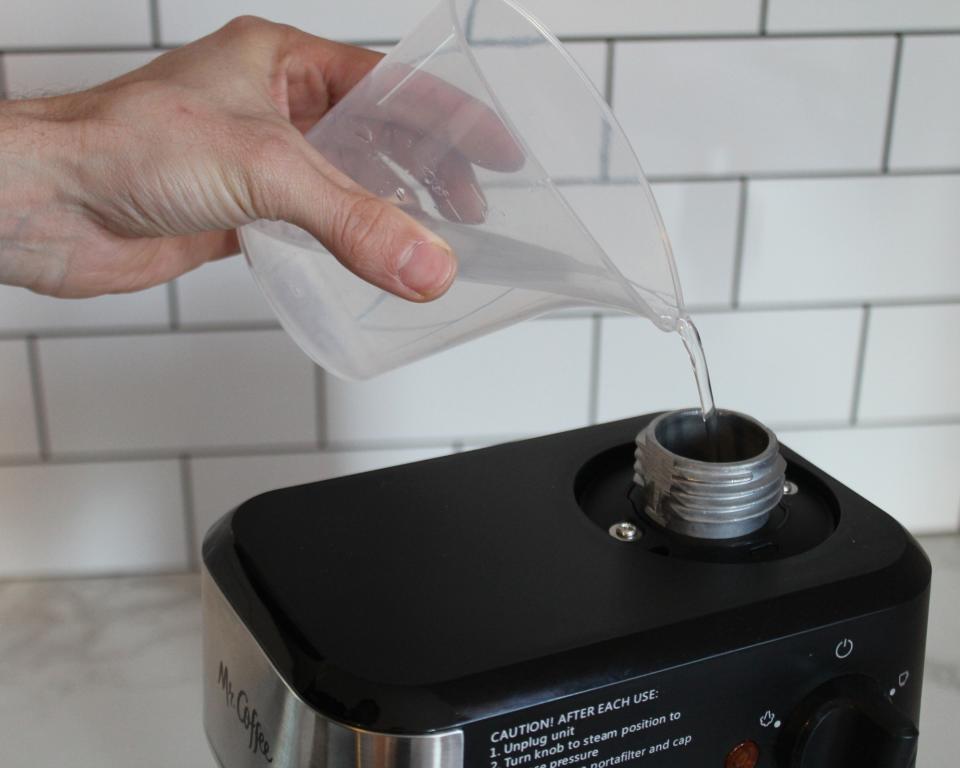 Camryn Rabideau, a caucasian woman using plastic measuring jug to fill Mr. Coffee Steam Espresso Maker machine