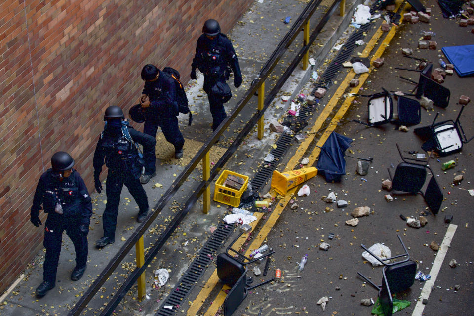 Policemen from Explosive Ordnance Disposal (EOD) unit walk by chairs and debris scattered on a road as they search for dangerous materials at the Hong Kong Polytechnic University campus in Hong Kong, Thursday, Nov. 28, 2019. Police safety teams Thursday began clearing a university that was a flashpoint for clashes with protesters, and an officer said any holdouts still hiding inside would not be immediately arrested. (AP Photo/Ng Han Guan)