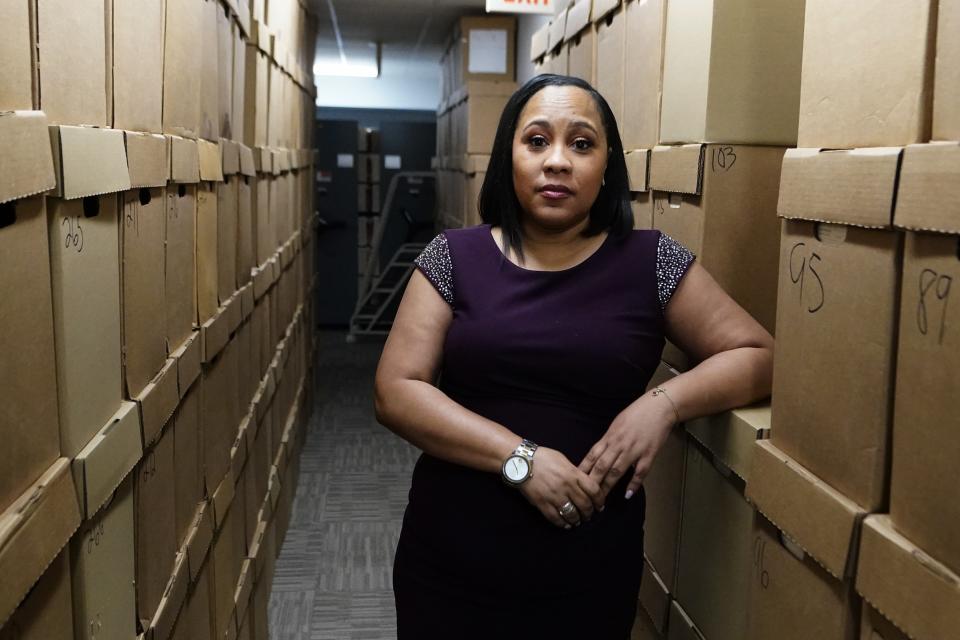 Fulton County District Attorney Fani Willis stands between two floor-to-ceiling rows of boxes, resting her elbow on one of them.