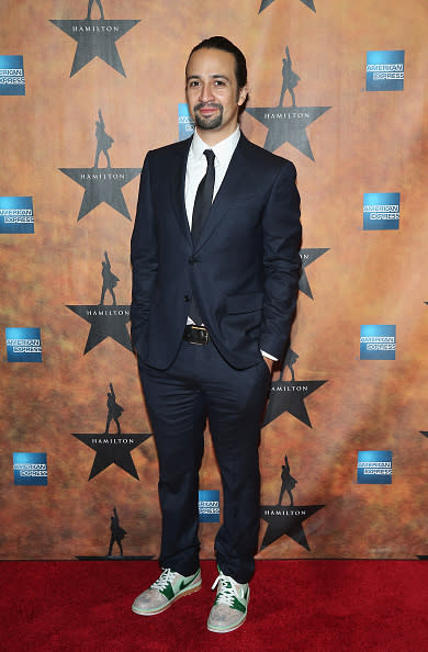 Lin-Manuel Miranda in a navy blue suit and sneakers.