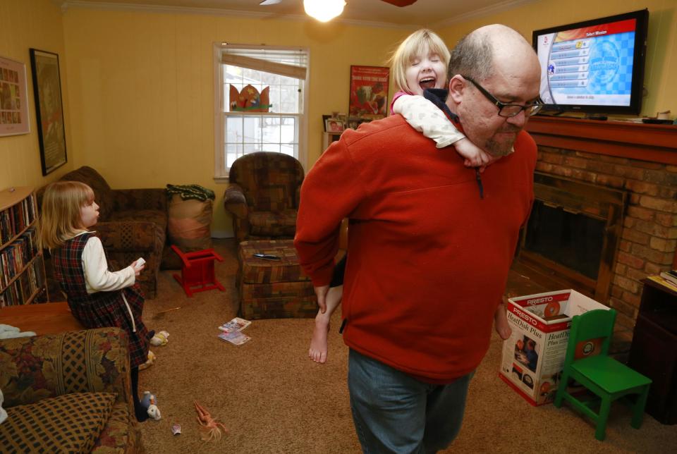 Mike Beck carries his daughter Veronica on his back through the family's living room as his daughter Maria, left, plays a video while trying to combat cabin fever, Monday, Feb. 3, 2014, in Indianapolis. (AP Photo/R Brent Smith)
