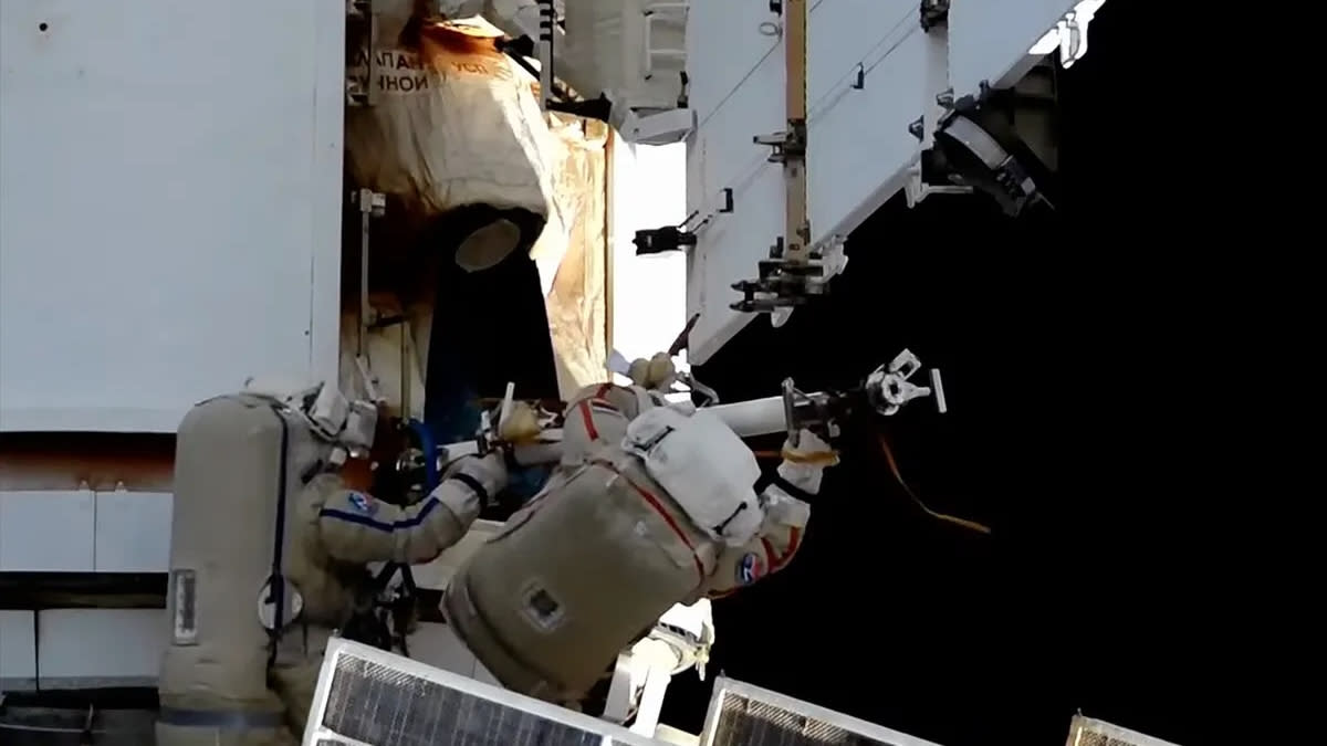  Two astronauts in white spacesuits work outside the international space station. 