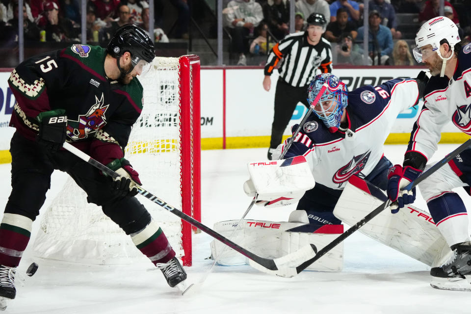 Columbus Blue Jackets goaltender Elvis Merzlikins, second from right, makes a save on a shot by Arizona Coyotes center Alex Kerfoot (15) as Blue Jackets defenseman Erik Gudbranson, right, skates to the puck during the first period of an NHL hockey game Tuesday, March 26, 2024, in Tempe, Ariz. (AP Photo/Ross D. Franklin)