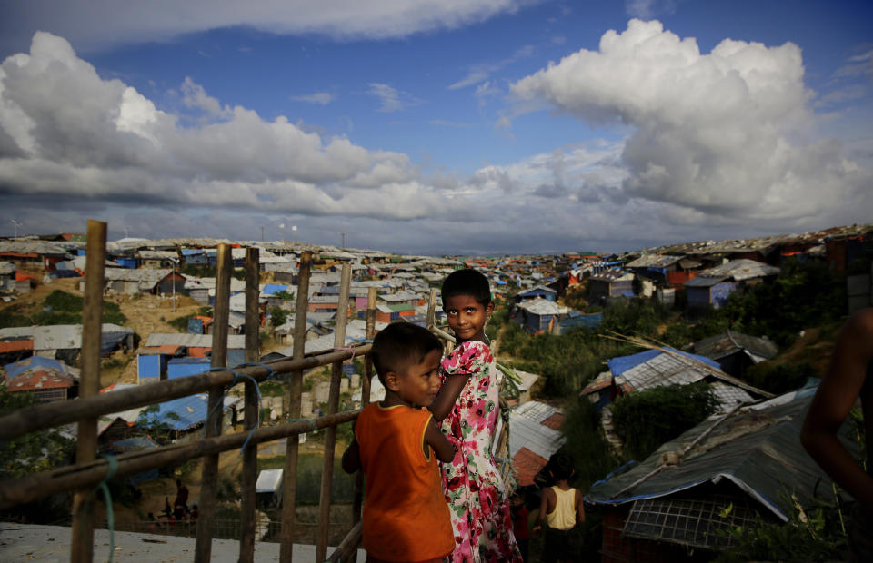 Rohingya children stand next to a bamboo fence overlooking an expanse of makeshift bamboo and tarp shelters at Kutupalong refugee camp, where they have been living amid uncertainty over their future after they fled Myanmar to escape violence a year ago, in Bangladesh, Sunday, Aug. 26, 2018. (AP Photo/Altaf Qadri)