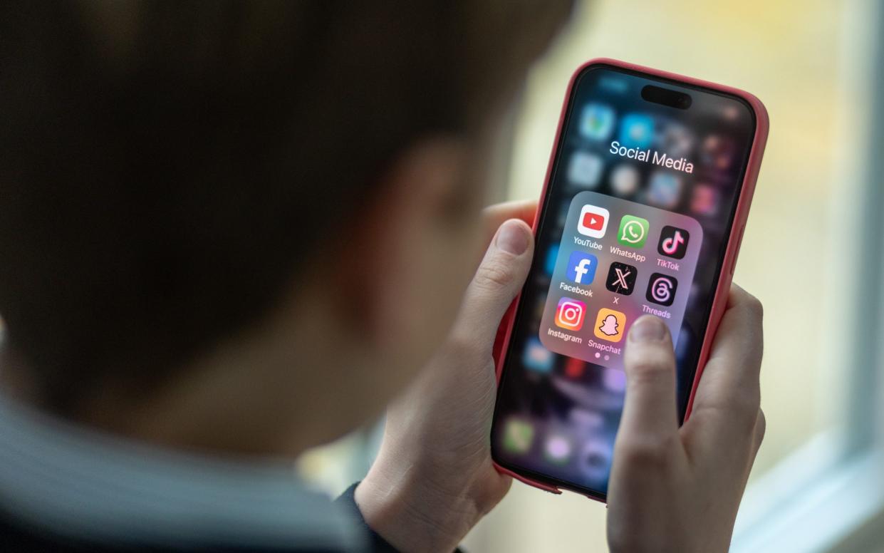 A 12-year-old boy looks at an iPhone screen showing various social media apps