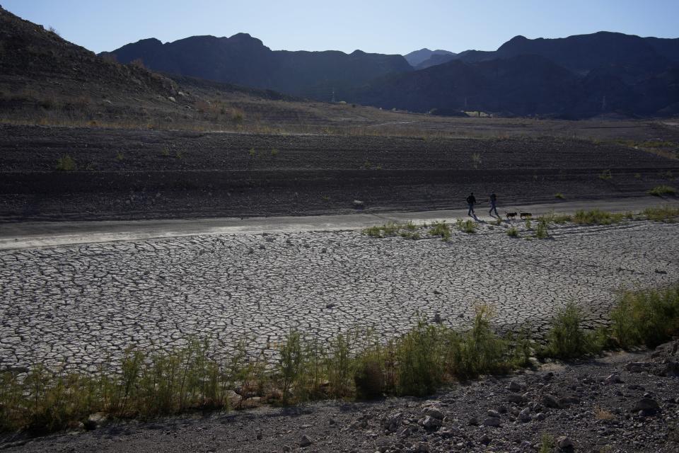 People walk by cracked earth in an area once under the water of Lake Mead at the Lake Mead National Recreation Area, Friday, Jan. 27, 2023, near Boulder City, Nev. Competing priorities, outsized demands and the federal government's retreat from a threatened deadline all combined to thwart a voluntary deal last summer on how to drastically cut water use from the parched Colorado River, according to emails obtained by The Associated Press. (AP Photo/John Locher)