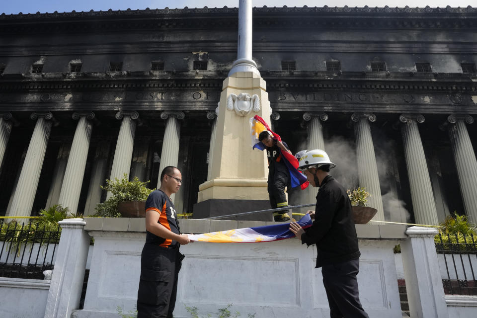 Firemen fold a Philippine flag in front of the Manila Central Post Office after it caught fire early Monday, May 22, 2023 in Manila, Philippines. A massive fire tore through Manila's historic post office building overnight, police and postal officials said Monday. (AP Photo/Aaron Favila)