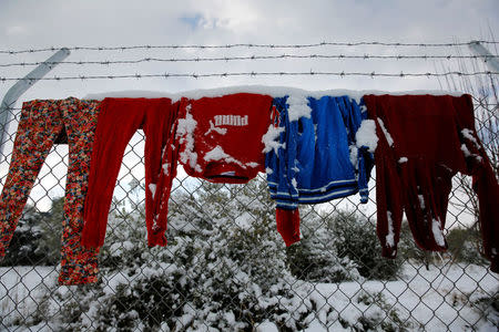 Clothes that belong to stranded refugees are covered with snow as they hang on a fence during a show storm at a refugee camp north of Athens, Greece January 10, 2017. REUTERS/Yannis Behrakis