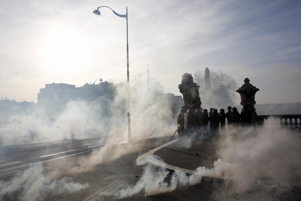 Riot police officers hide behind statues amid tear gas canisters during a demonstration Saturday, Feb.16, 2019 in Paris. Hundreds of yellow vest protesters marched through Paris, one of seven scattered demonstrations in the French capital Saturday, for the 14th straight weekend. (AP Photo/Thibault Camus)