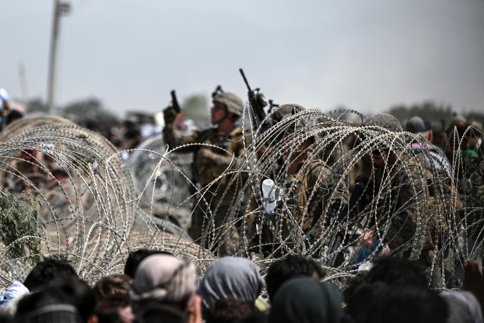 A US soldier shoots in the air with his pistol whiel standing guard behind barbed wire as Afghans sit on a roadside near the military part of the airport in Kabul on August 20, 2021, hoping to flee from the country after the Taliban's military takeover of Afghanistan. (Photo by Wakil KOHSAR / AFP) (Photo by WAKIL KOHSAR/AFP via Getty Images)