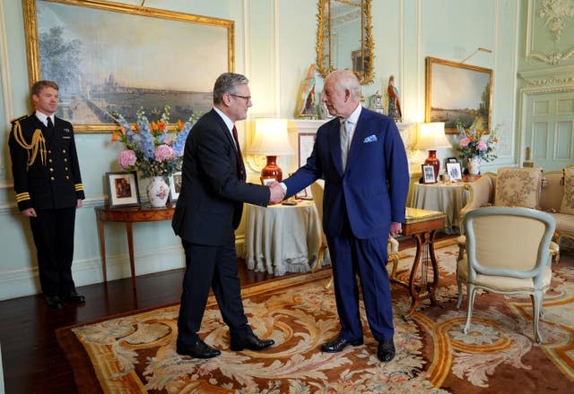 Sir Keir Starmer shakes hands with the King in a richly decorated room while an official looks on