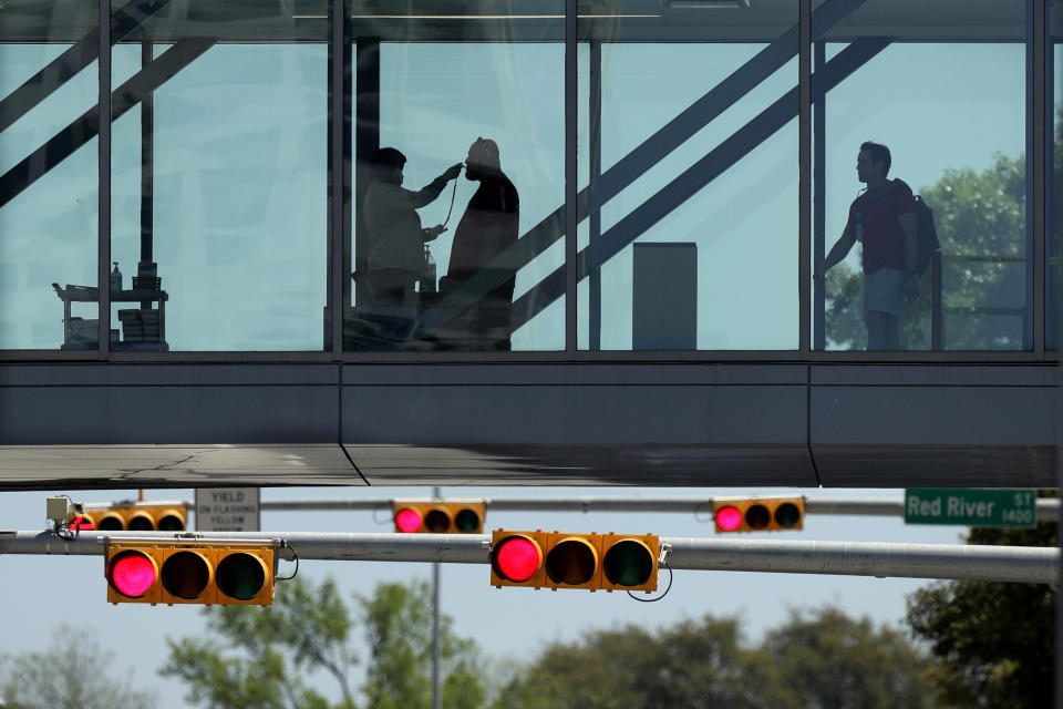 A man has his temperature taken at a control point on a covered footbridge to be screened for symptoms before entering the Dell Deton Medical Center at the University of Texas in Austin, Texas, Wednesday, March 25, 2020. Austin is under Stay-at-Home orders to help battle the effects of COVID-19. (AP Photo/Eric Gay)