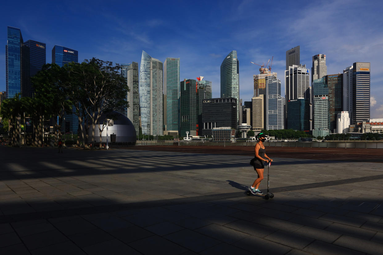 SINGAPORE - JUNE 07:  A woman wearing a protective mask rides a skate scooter along the Marina Bay waterfront with the central business district seen in the background on June 7, 2020 in Singapore. From June 2, Singapore embarked on phase one of a three phase approach against the coronavirus (COVID-19) pandemic as it began to ease the partial lockdown measures by allowing the safe re-opening of economic activities which do not pose high risk of transmission. This include the resumption of selected health services, re-opening of schools with school children attending schools on rotational basis, manufacturing and production facilities, construction sites that adhere to safety measures, finance and information services that do not require interactions and places of worship, amongst others. Retail outlets, social and entertainment activities will remain closed and dining in at food and beverage outlets will still be disallowed. The government will further ease restriction by the middle of June if the infection rate within the community remains low over the next two weeks.  (Photo by Suhaimi Abdullah/Getty Images)