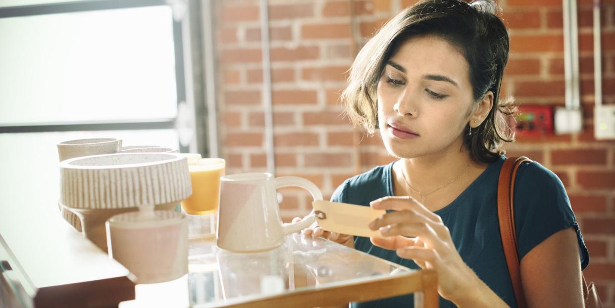 woman in a shop, looking at the price tag of a white ceramic mug