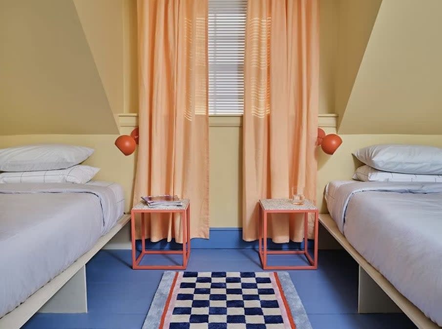 Two twin beds under a dormered ceiling with peach curtains, room painted in Miami Parasol by Backdrop.