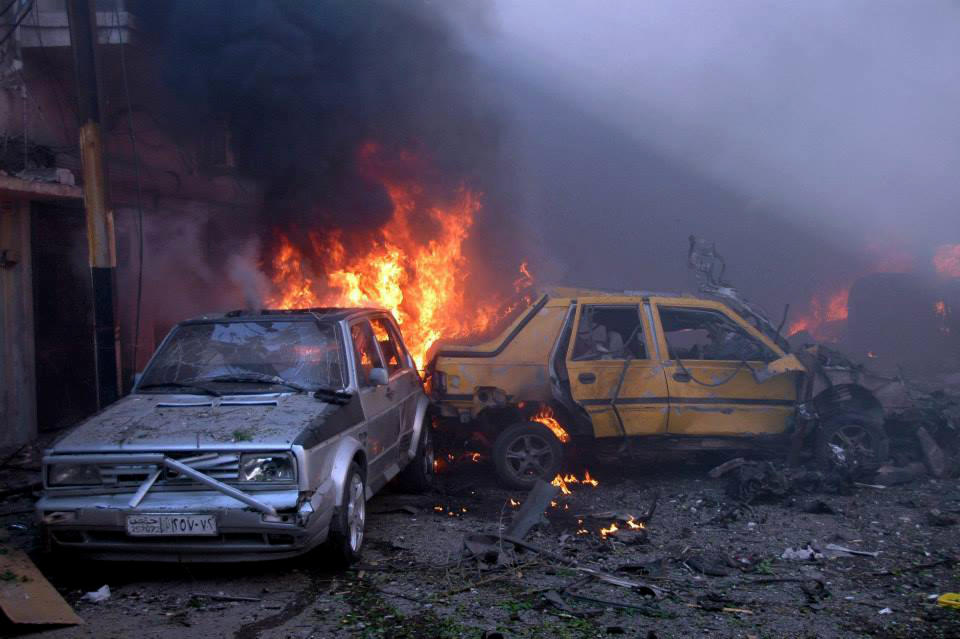 In this photo released by the Syrian official news agency SANA, Flames rise from damaged cars at the site where two car bombs exploded at a commercial street inhabited mostly by members of President Bashar Assad's minority Alawite sect, in Homs province, central Syria, Wednesday April 9, 2014. Two car bombs exploded Wednesday in a government-held district of Syria's battleground city of Homs, killing at least 25 people and wounding more than 100, state media said. (AP Photo/SANA)