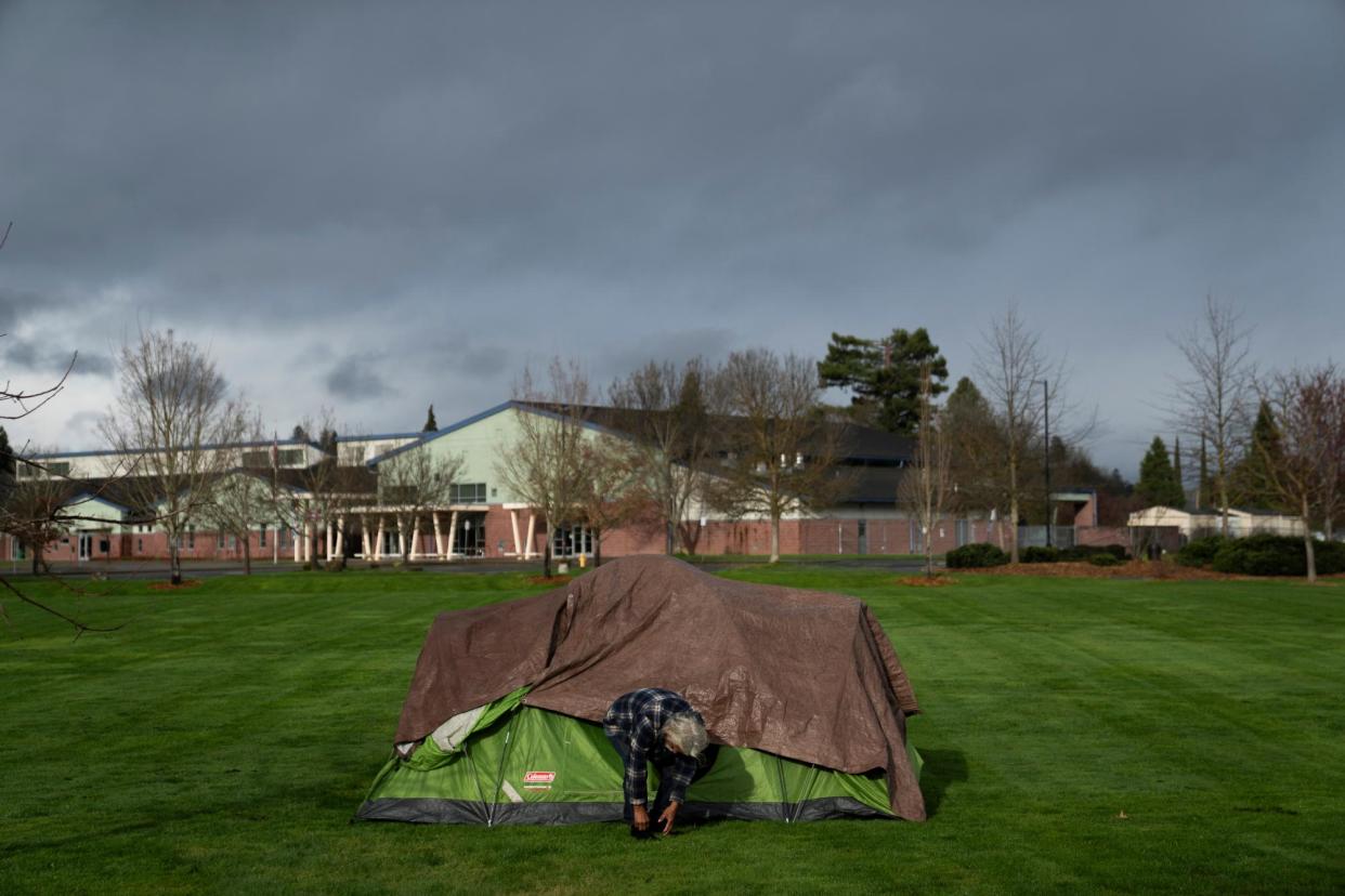 <span>With Fruitdale Elementary School in the background, a homeless man adjusts his shoe at Fruitdale Park in Grants Pass, Oregon, on 23 March.</span><span>Photograph: Jenny Kane/AP</span>