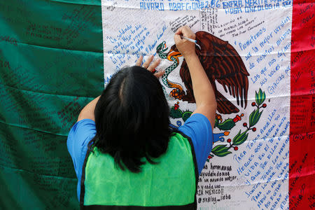 A woman writes a message on Mexico's flag before a homage to the victims of a building that collapsed during the September 2017 earthquake in Mexico City, Mexico September 19, 2018. REUTERS/Gustavo Graf