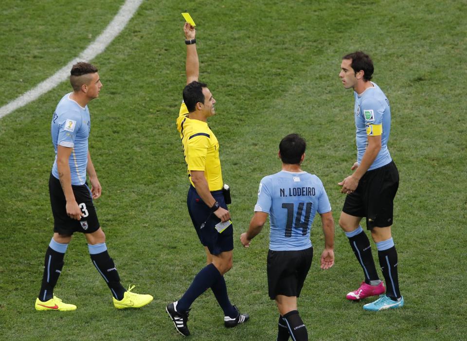 Uruguay's Godin receives a yellow card from referee Carballo of Spain during their 2014 World Cup Group D soccer match against England at the Corinthians arena in Sao Paulo