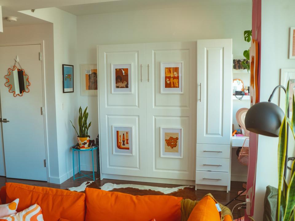 Four orange and red abstract prints hang on the exterior of a folded up murphy bed