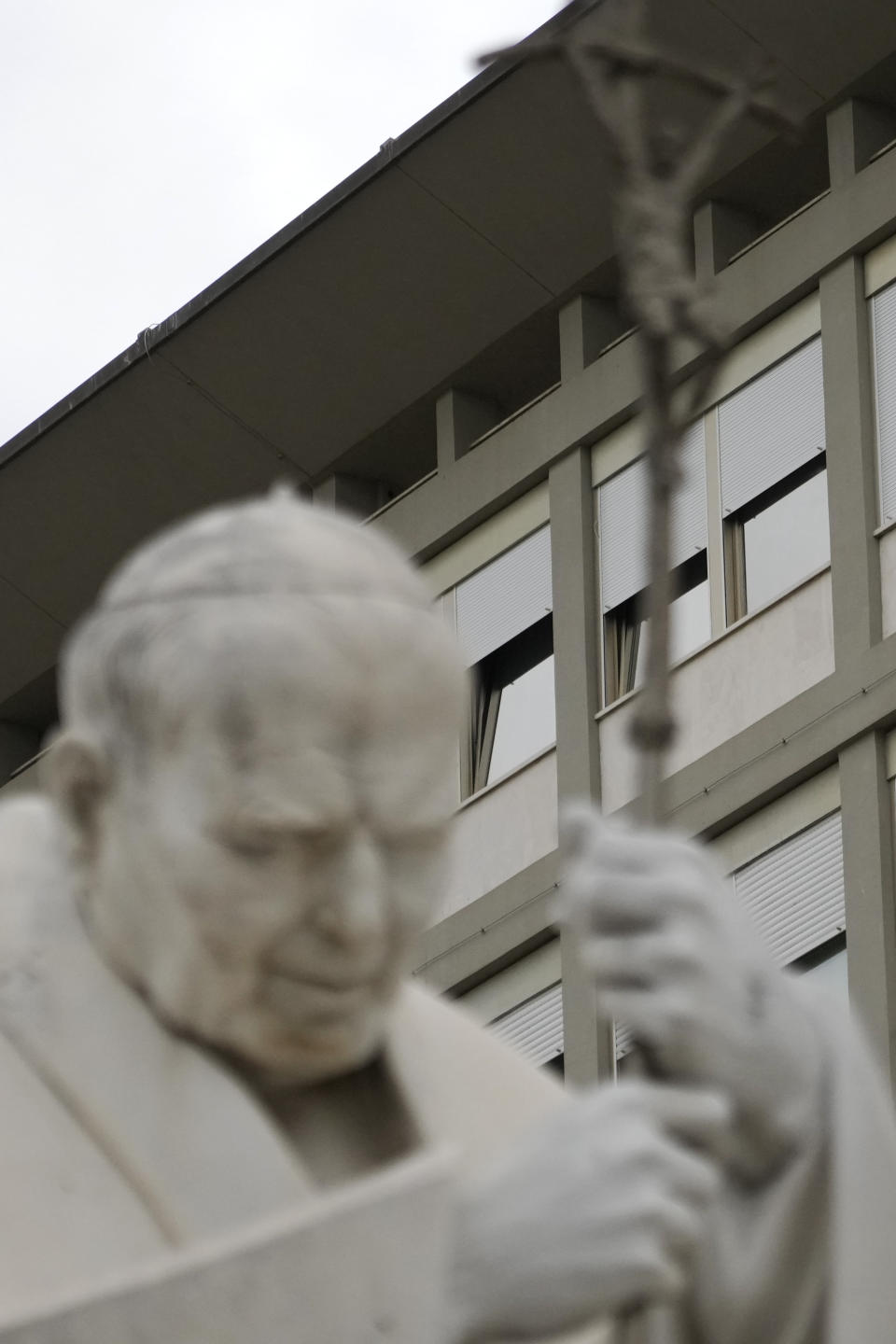 A statue of late Pope John Paul II is backdropped by the rooms on the top floor normally used when a pope is hospitalised at the Agostino Gemelli hospital, in Rome, Friday, March 31, 2023. Pope Francis spent another night in hospital after showing a "marked improvement" Thursday and could be released from the hospital in the coming days, the Vatican and his doctors reported. (AP Photo/Gregorio Borgia)