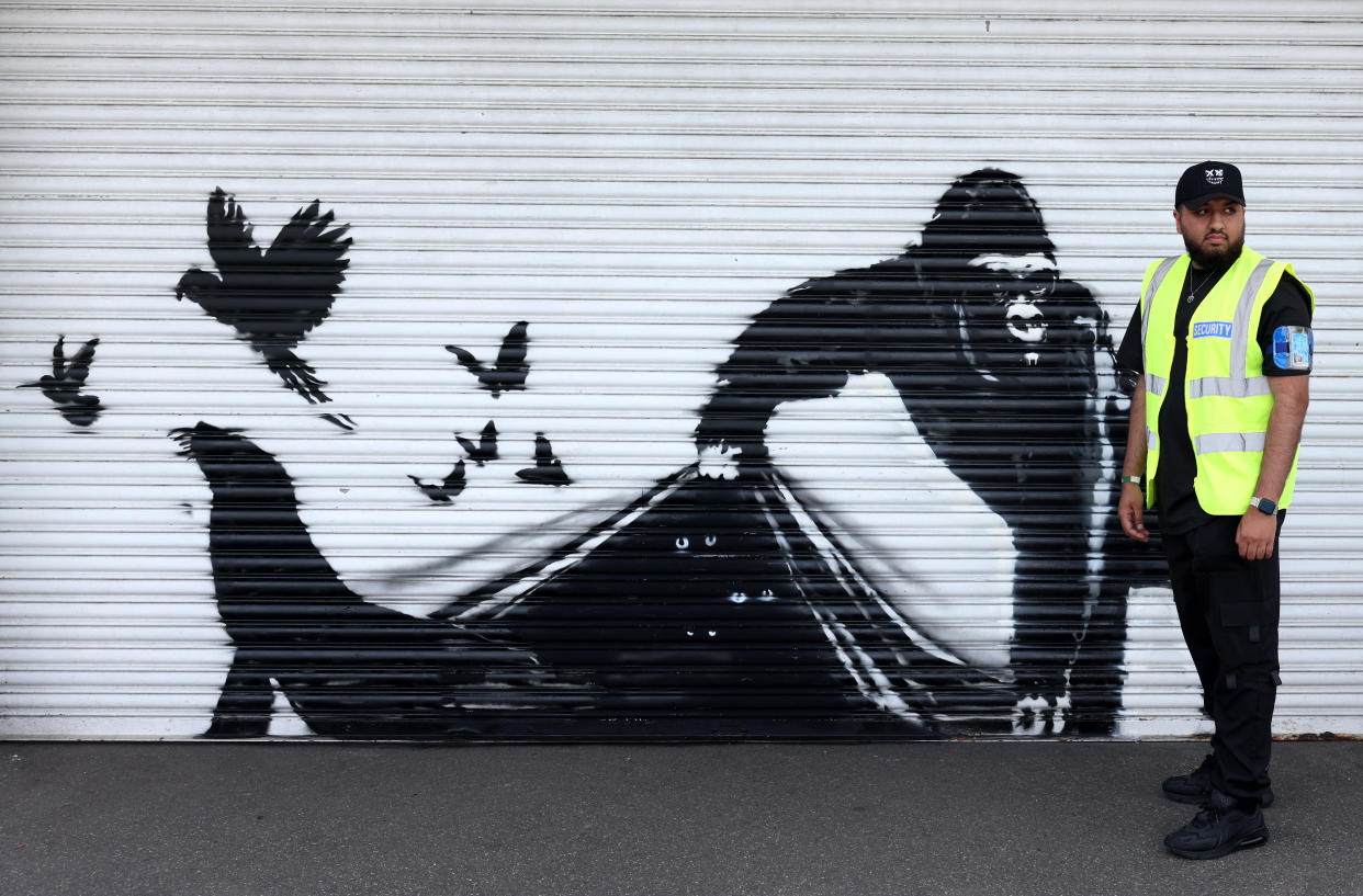 A security guard stands beside an artwork by street artist Banksy, the ninth to released in nine days, depicting a gorilla releasing animals, on the front of a shutter outside London zoo, on August 13, 2024. The artist confirmed the work to be theirs after posting an image of it on the social media app Instagram.gor (Photo by Adrian DENNIS / AFP) / RESTRICTED TO EDITORIAL USE - MANDATORY MENTION OF THE ARTIST UPON PUBLICATION - TO ILLUSTRATE THE EVENT AS SPECIFIED IN THE CAPTION (Photo by ADRIAN DENNIS/AFP via Getty Images)