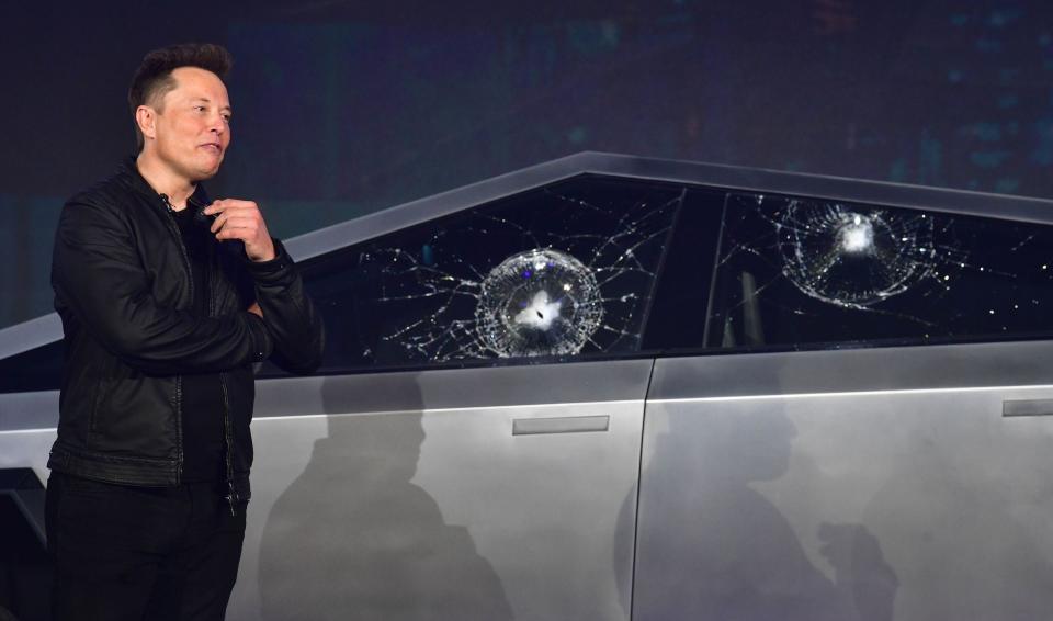 Elon Musk standing next to a cybertruck with smashed windows.