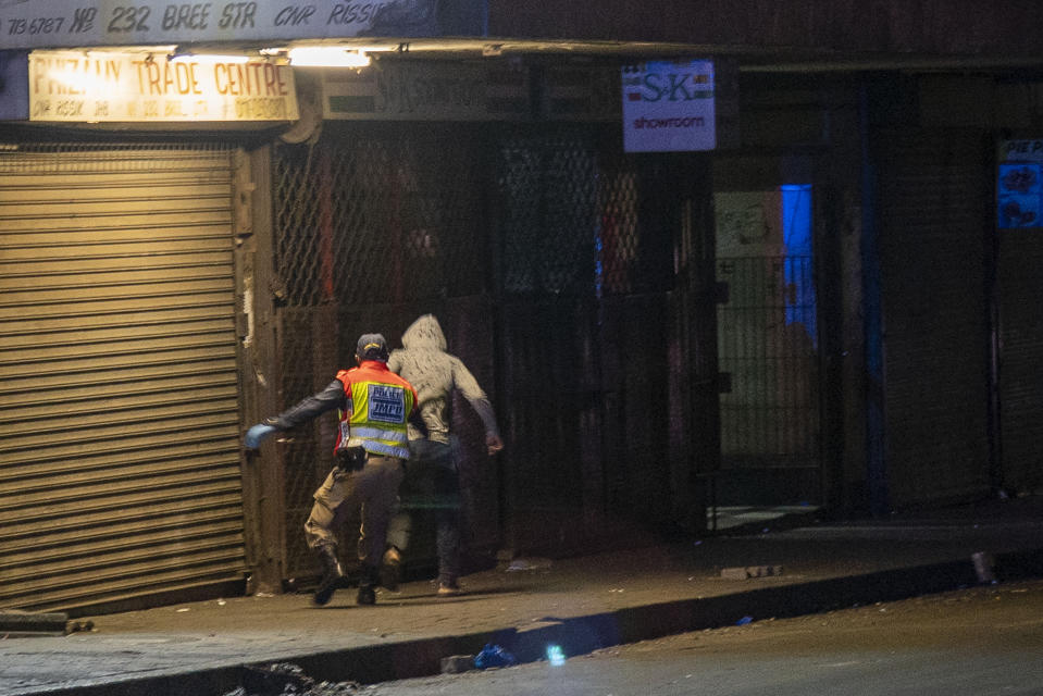 A police officer chases a man who violated the lockdown downtown Johannesburg, South Africa, Friday, March 27, 2020. Police and army started patrolling moments after South Africa went into a nationwide lockdown for 21 days in an effort to mitigate the spread to the coronavirus. The new coronavirus causes mild or moderate symptoms for most people, but for some, especially older adults and people with existing health problems, it can cause more severe illness or death.(AP Photo/Jerome Delay)