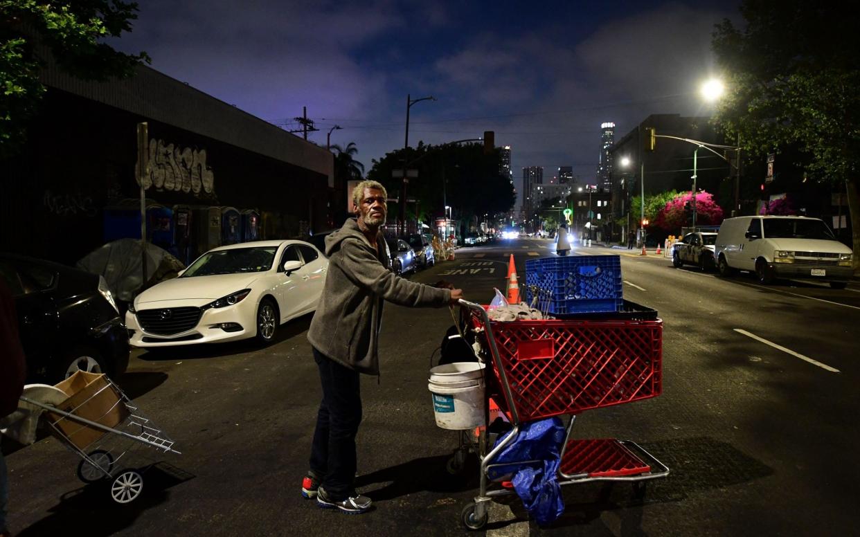 A homeless man pushes his cart of belongings along the streets of downtown Los Angeles, California - AFP