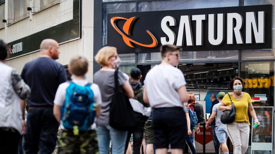 Menschen stehen in einer Warteschlange in Köln vor einer Filiale des Elektrohändlers Saturn an.