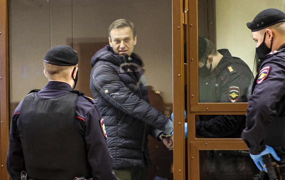 In this photo taken from a footage provided by the Babuskinsky District Court Tuesday, Feb. 16, 2021, Russian opposition leader Alexei Navalny, center, enters a cage to attend a hearing on his charges for defamation in the Babuskinsky District Court in Moscow, Russia. Navalny is accused of defaming a World War II veteran who was featured in a video last year advertising constitutional amendments that allowed an extension of President Vladimir Putin's rule. (Babuskinsky District Court Press Service via AP)