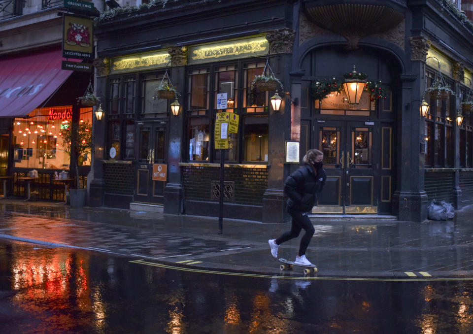 A man wears a face mask as she skates past a closed pub in Soho, in London, Wednesday, Dec. 16, 2020. London and some of its surrounding areas will be placed under Britain's highest level of coronavirus restrictions beginning at 00:01 local time on today as infections rise rapidly in the capital. Under Tier 3 restrictions, the toughest level in England's three-tier system, people can't socialize indoors, and bars, pubs and restaurants must close except for takeout.(AP Photo/Alberto Pezzali)