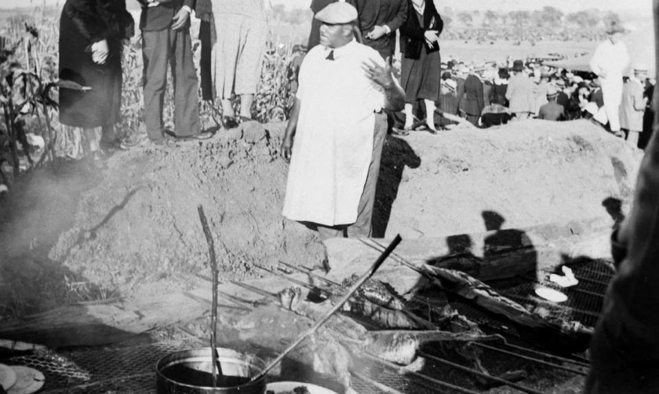 A local pitmaster tends a barbecue pit dug into the ground.