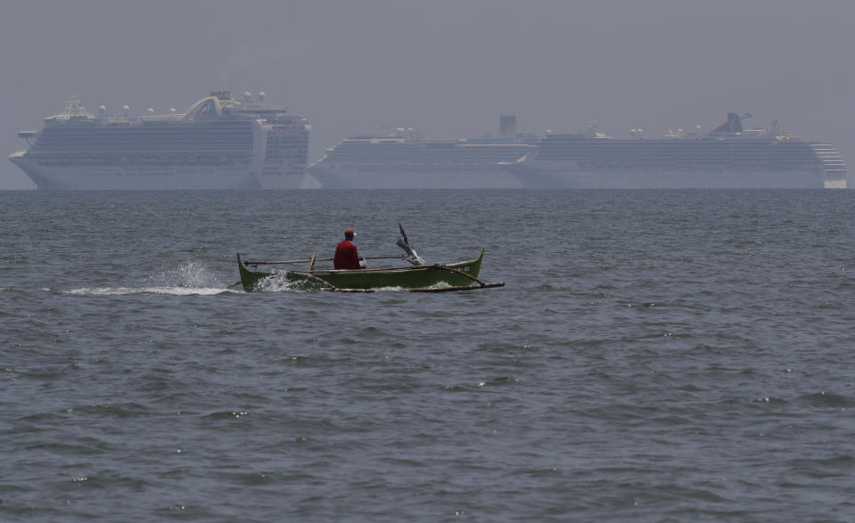 A fishing boat passes in front of the Ruby Princess cruise ship, left, and other ships as they are anchored in the Manila Bay, Philippines, Thursday, May 7, 2020. The Ruby Princess which is being investigated in Australia for sparking coronavirus infections, has sailed into Philippine waters to bring Filipino crewmen home. (AP Photo/Aaron Favila)