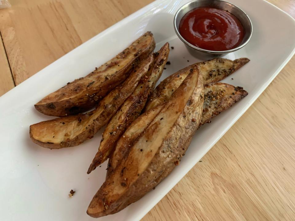 Air fried potato wedges on a white plate with ketchup on the side