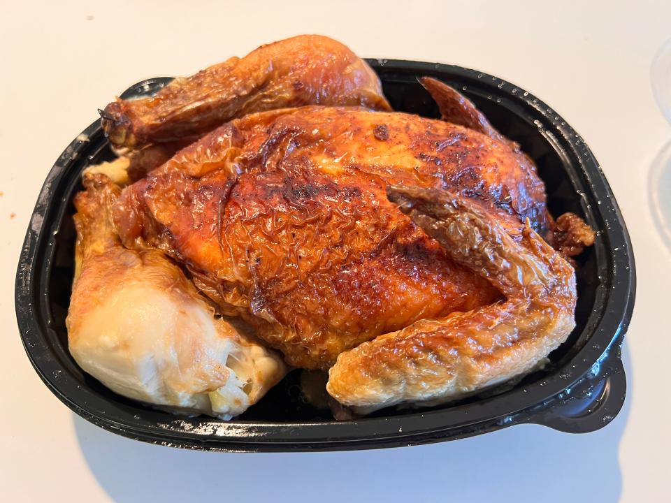 A rotisserie chicken sits in a black container on a white counter