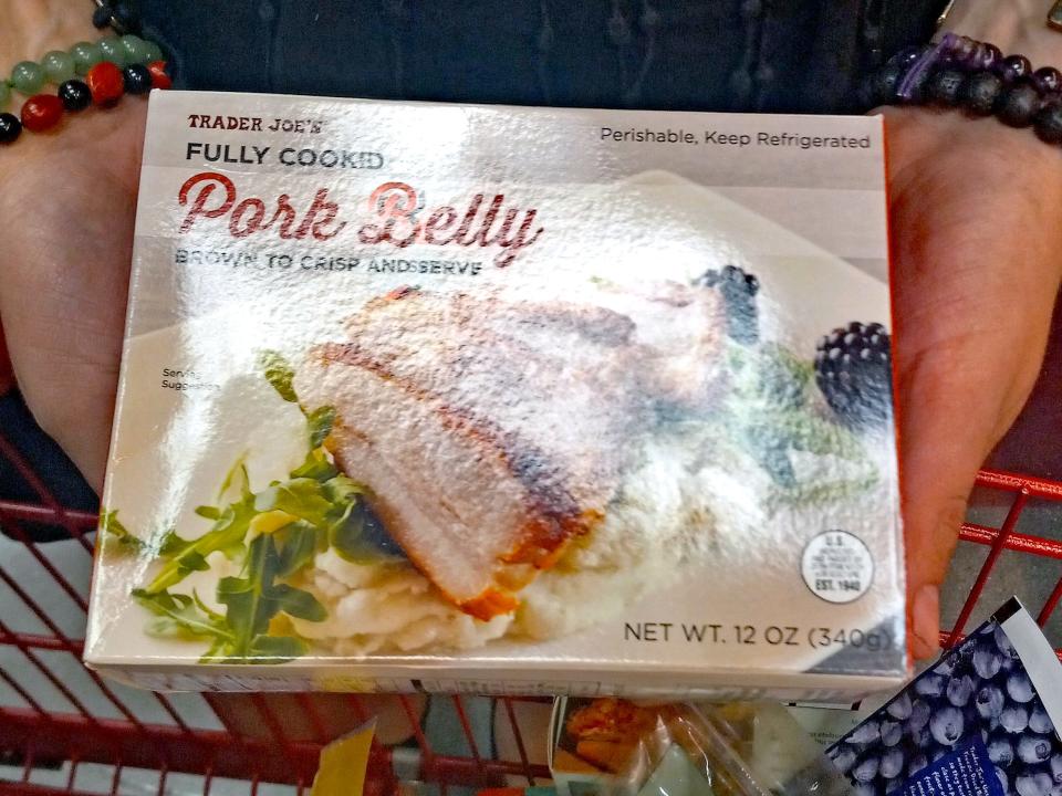 hands holding box of pork belly in an aisle of trader joes