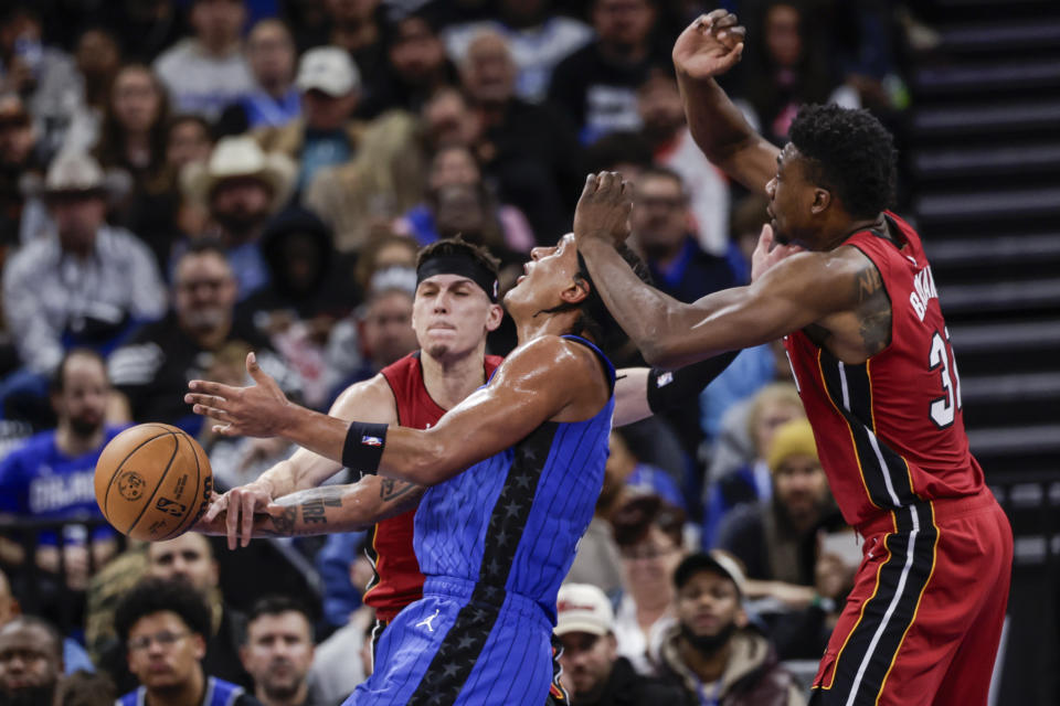 Orlando Magic forward Paolo Banchero, middle, is defended by Miami Heat guard Tyler Herro, left, and center Thomas Bryant, right, during the first half of an NBA basketball game, Wednesday, Dec. 20, 2023, in Orlando, Fla. (AP Photo/Kevin Kolczynski)