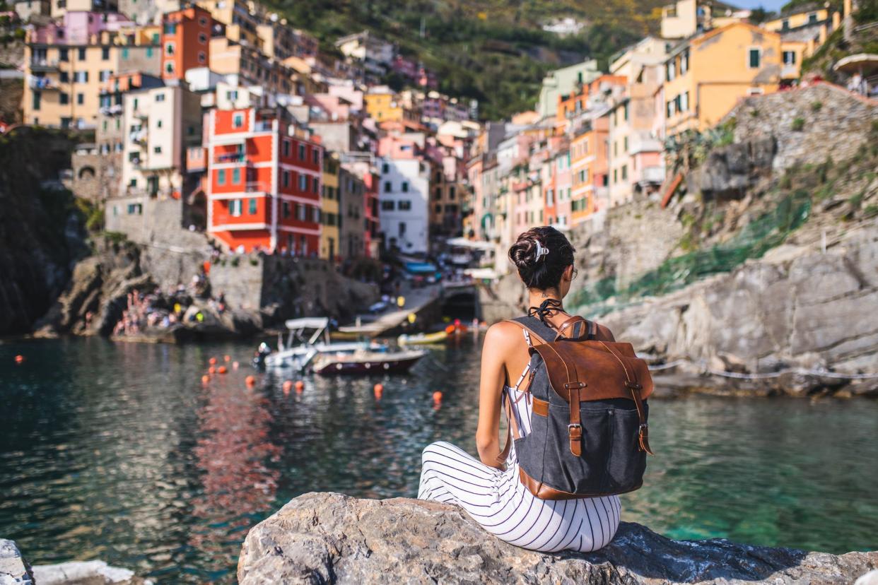 Female tourist relaxing by the sea. She is looking at the beautiful town Riomaggiore, Cinque Terre