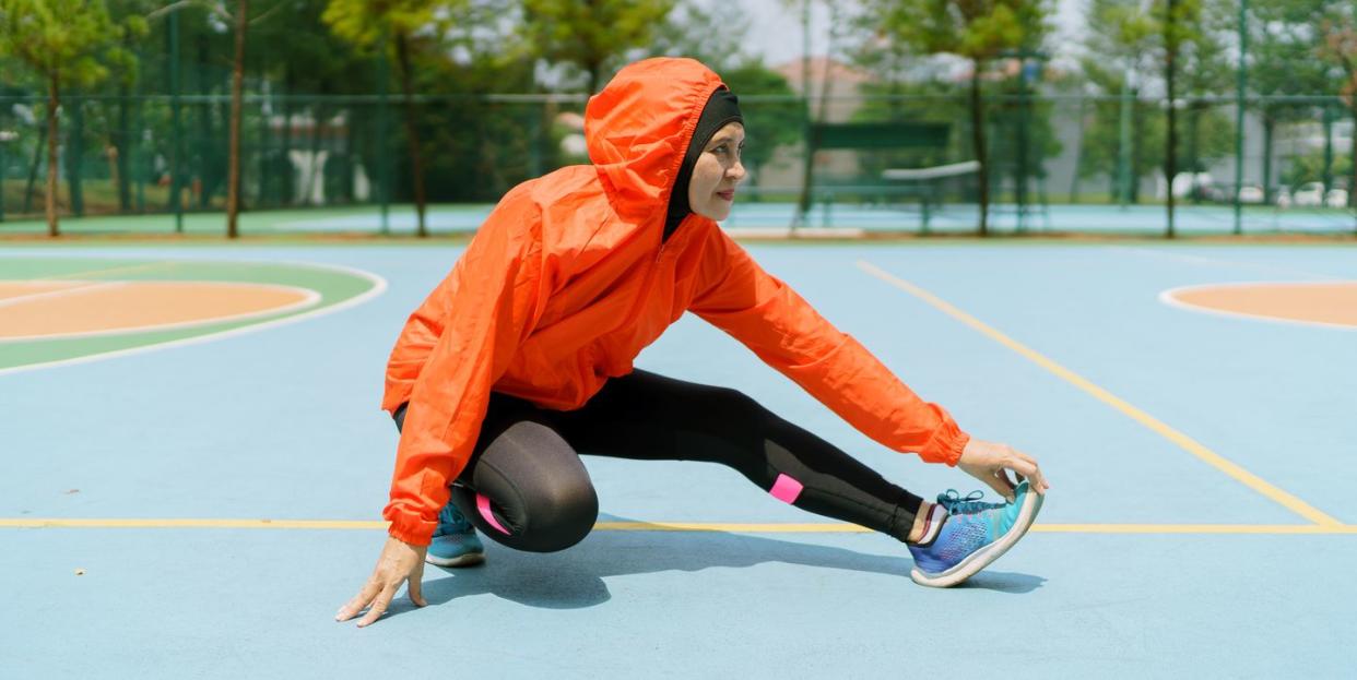 sporty muslim woman and runner with hijab stretching legs in the park