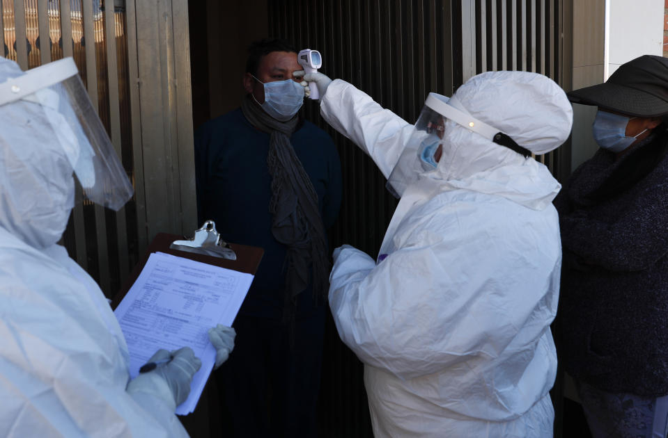 A doctor, dressed in full protective gear, measures the temperature of resident during a house-to-house new coronavirus testing campaign in the Villa Jaime Paz Zamora neighborhood of El Alto, Bolivia, Saturday, July 4, 2020. (AP Photo/Juan Karita)