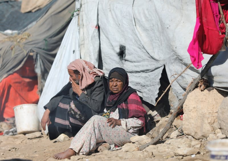 People sit in the sun on a cold winter day at a camp for internally displaced people in Khamir of the northwestern province of Amran