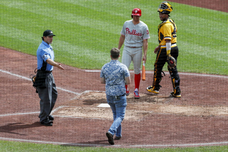 Home plate umpire Ben May, left, looks at a man walking towards Pittsburgh Pirates catcher Elias Diaz, right and Philadelphia Phillies' Brad Miller as he comes to bat in the sixth inning of a baseball game, Sunday, July 21, 2019, in Pittsburgh. The police took the man from the field and play continued. (AP Photo/Keith Srakocic)