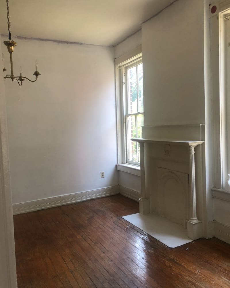 Empty white room (living room? bedroom?) with mantel with thin columns, wood flooring and gold chandelier.