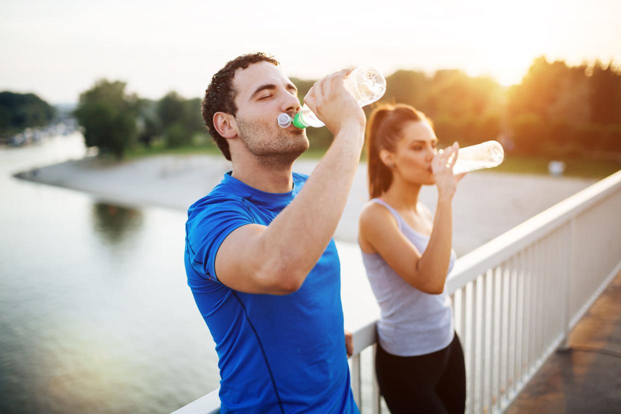 couple outside drinking water from water bottle while taking a break from exercising