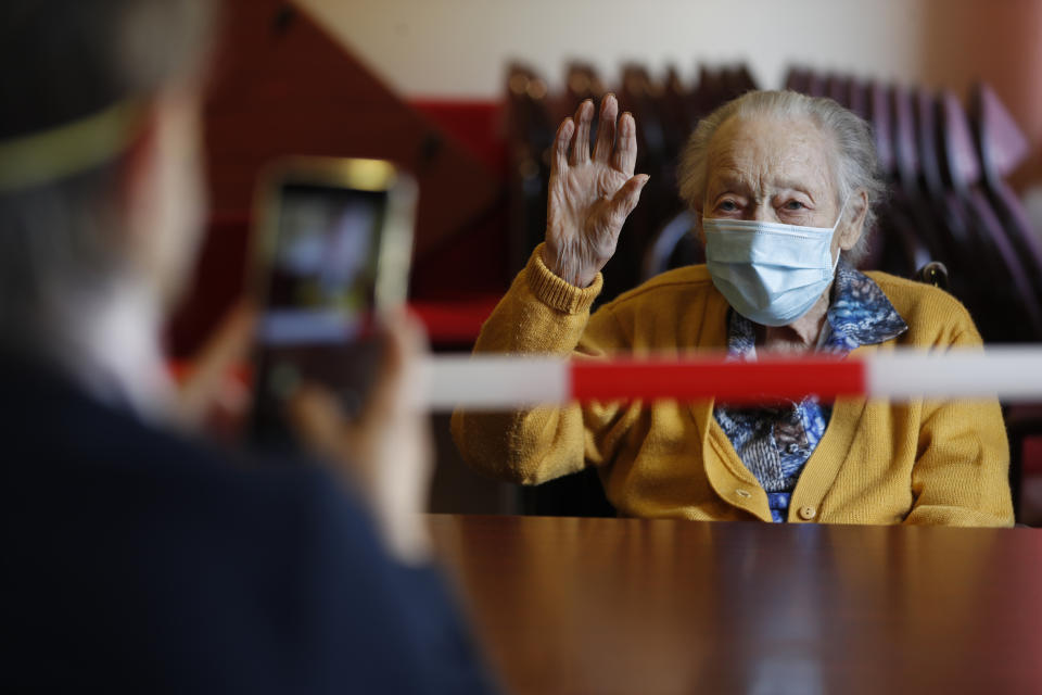 In this April 21, 2020, photo, Marguerite Mouille, 94, gestures while her visiting daughter takes a photo at the Kaisesberg nursing home, eastern France. France has started to break the seals on its locked down nursing homes, allowing limited visitation rights for the families of elderly residents. The visits are proving bittersweet for some, too short and restricted to make up for weeks of isolation and loneliness. But they are shedding light on the immense emotional toll caused by locking down care homes. (AP Photo/Jean-Francois Badias)