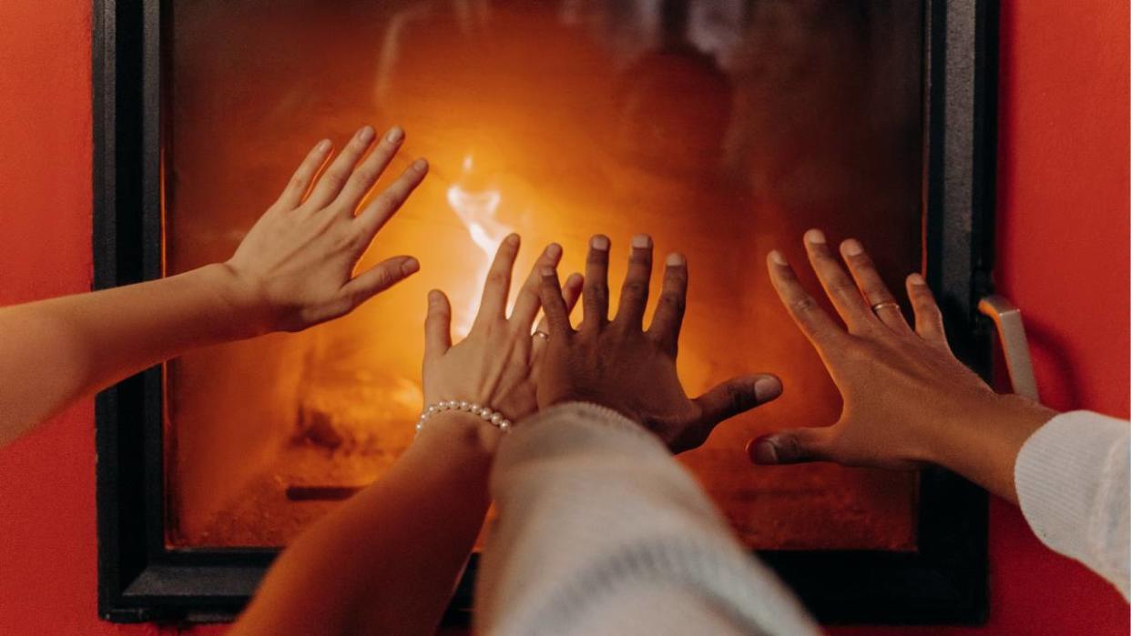  Four hands warming themselves in front of a fire. 