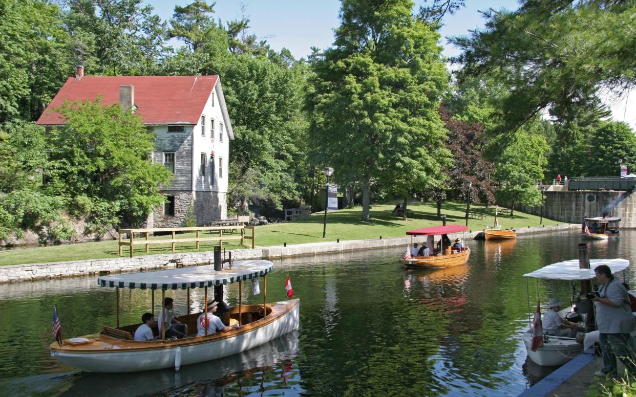 flotilla boats on water next to white wooden house with red roof and trees - Le Boat