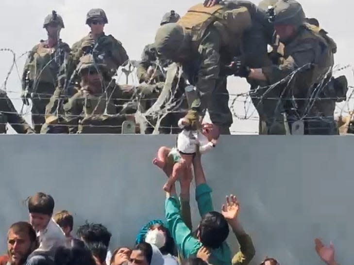 A baby is grabbed by a US soldier and lifted over a razor wire fence.