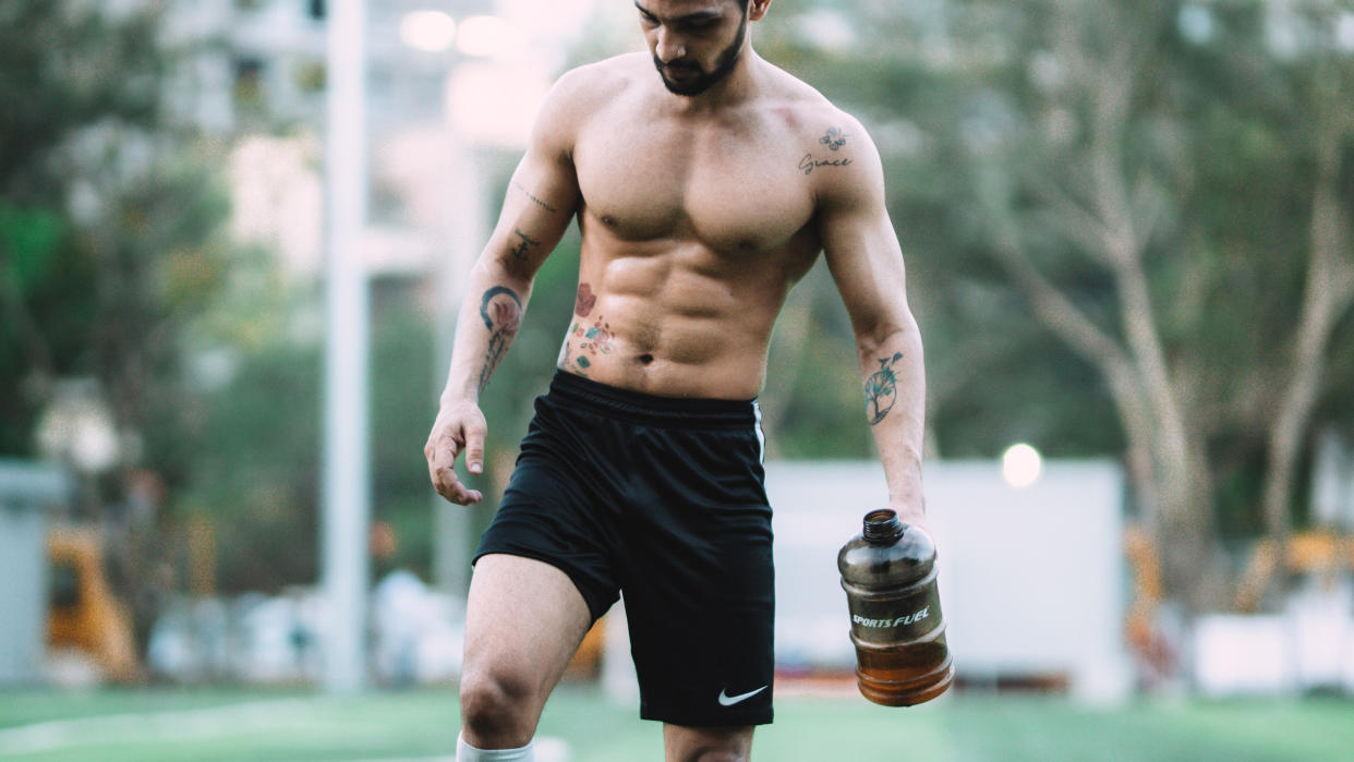  Man with a six-pack walking holding a water bottle. 